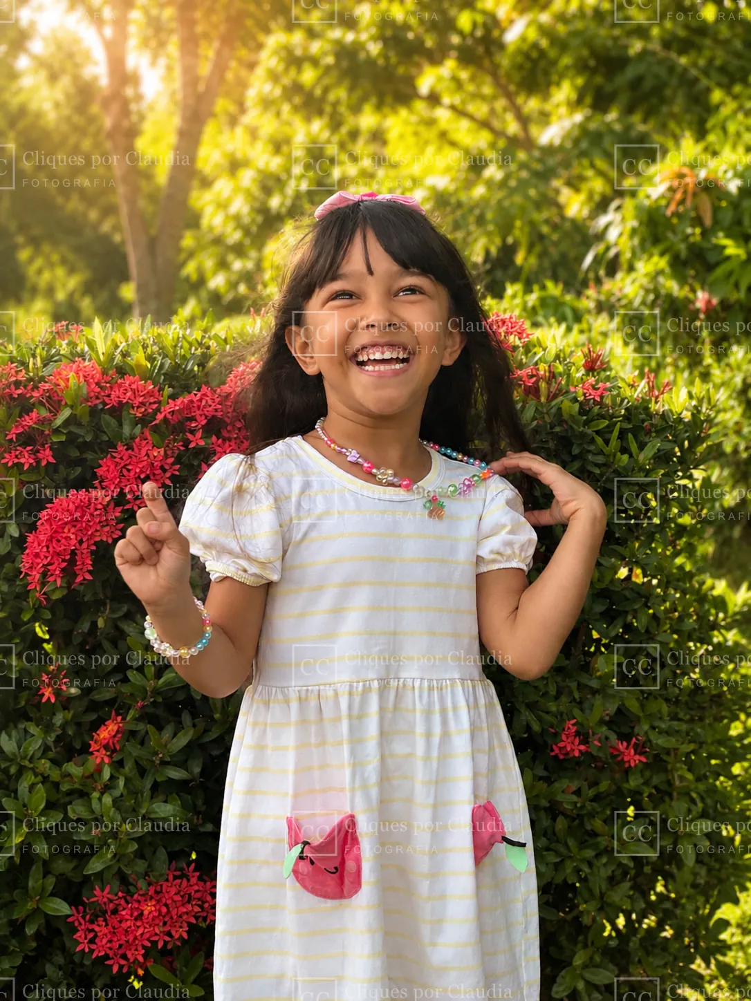 Maria Lívia gargalhando entre as flores no fim da tarde — ensaio infantil na Praia do Paiva